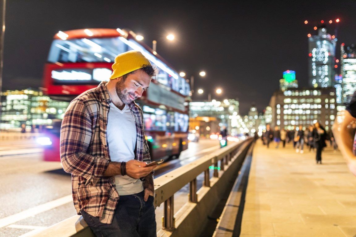 UK, London, smiling man using phone at the street in the city at night
