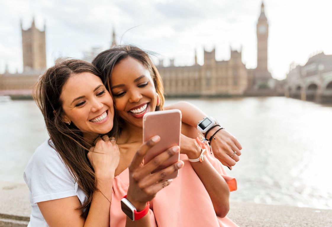 UK, London, two happy women with smartphone near Westminster Bridge
