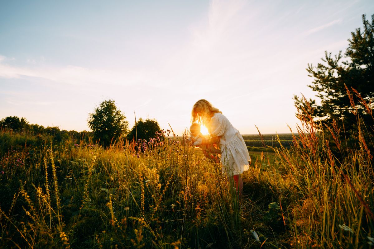 Mother showing wildflowers to baby daughter at sunset in a meadow summer nyár sunny forróság