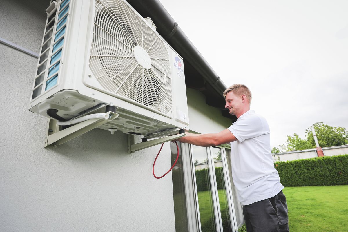 klíma kültéri egység szerelése, egy fehér polós férfival